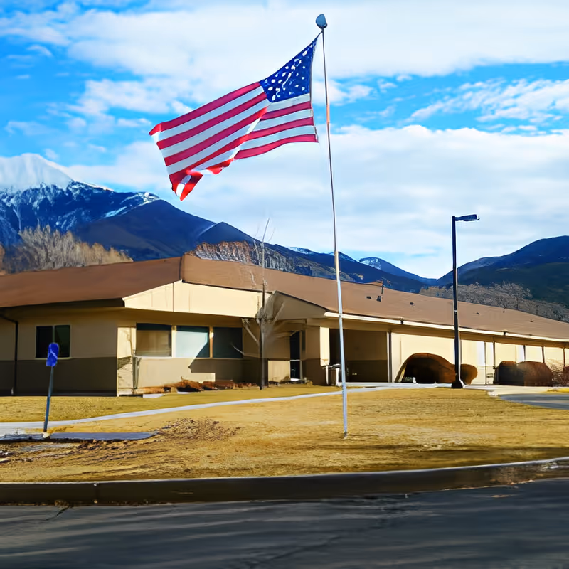 Single-story building with an American flag on a pole in front and mountains in the background.