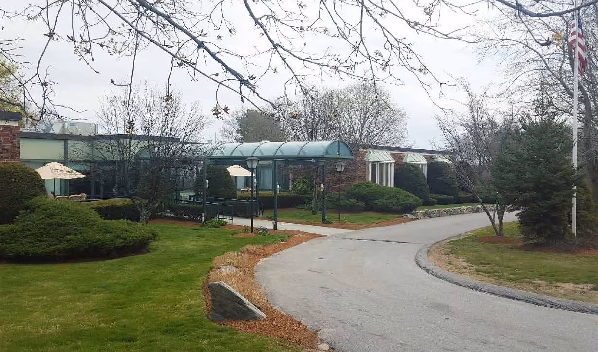 Driveway curves to the entrance of a low-rise brick rehabilitation center with a glass-covered walkway and landscaped grounds.