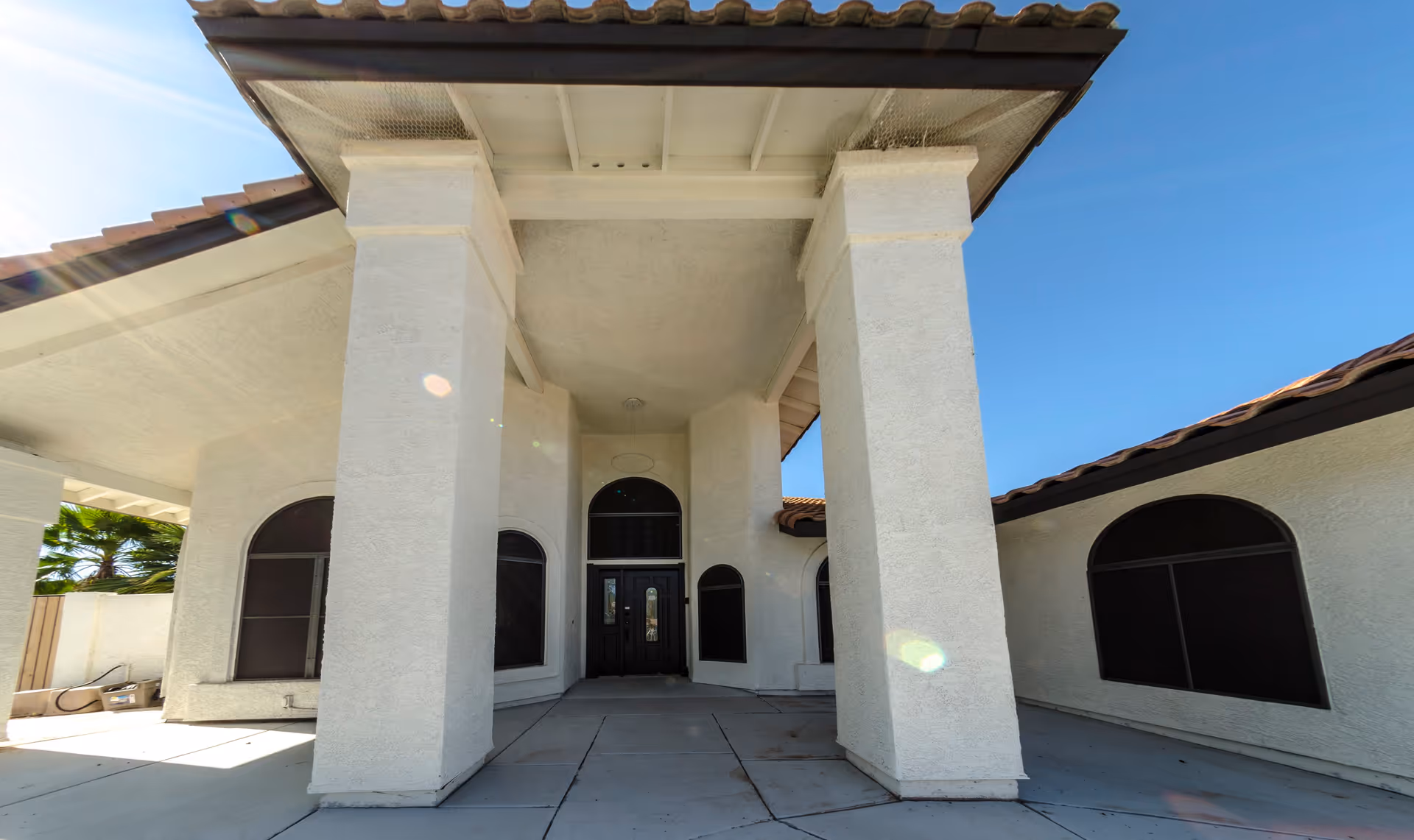 Front entrance of a stucco house with large columns, arched windows, and double doors under a covered portico.