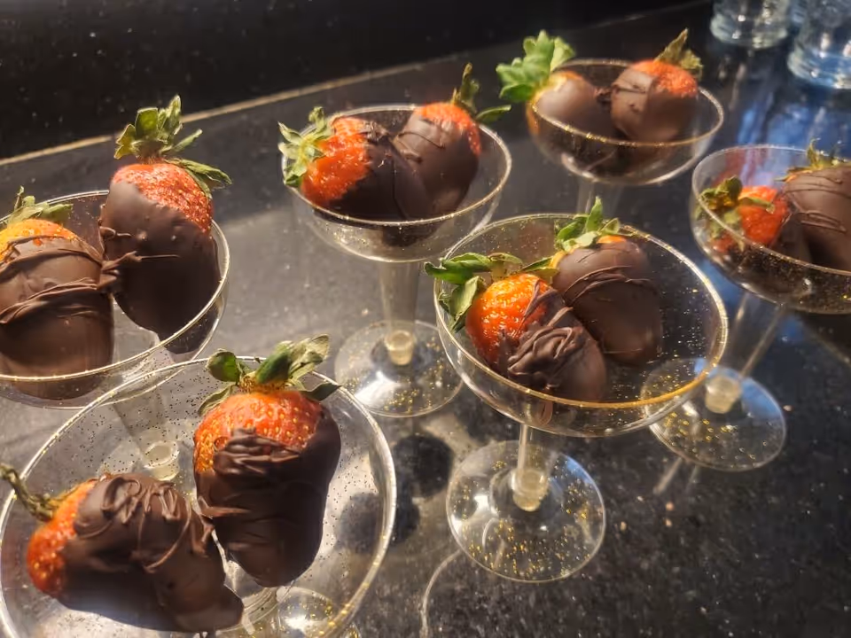 Chocolate-covered strawberries arranged in small glass dessert cups on a dark countertop.