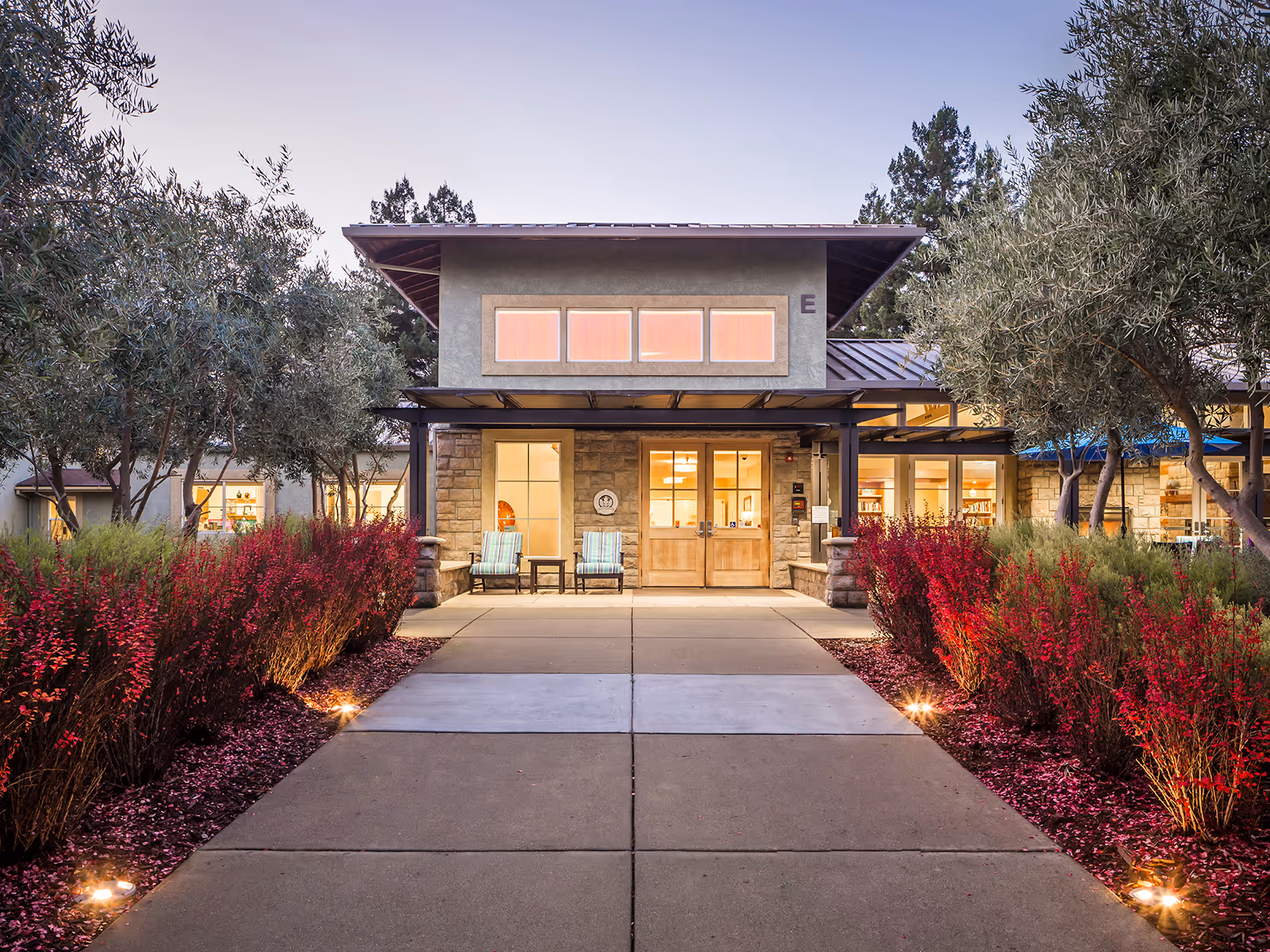 Front entrance of a senior living facility with stone facade, glass doors, and landscaped walkway.