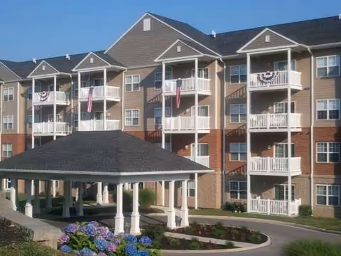 A multi-story senior living building with white balconies and a covered front pavilion, landscaped surroundings.
