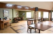 Interior dining area with multiple tables, chairs, and a piano in a warm, open space.