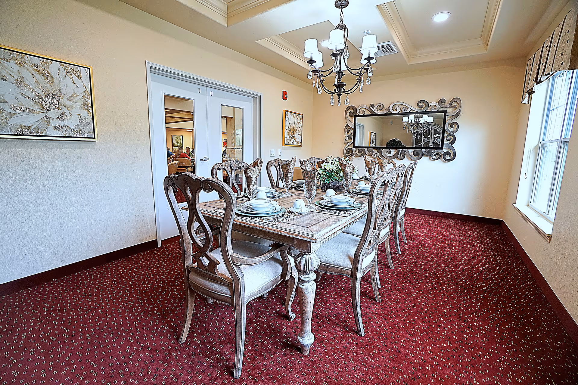 Formal dining room with an ornate wooden table set with dishes, matching chairs, a chandelier, and a decorative wall mirror.