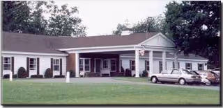 Front exterior of Madigan Estates Nursing Home with a covered entrance and parked cars.