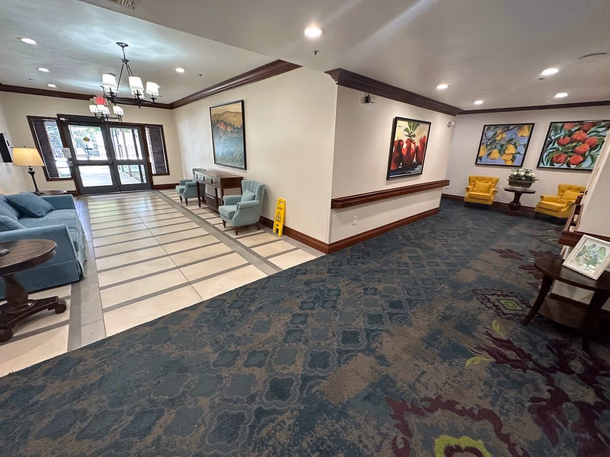Lobby seating area with sofas and armchairs, decorative carpet and tile pathway, artwork on the walls, and glass entrance doors.