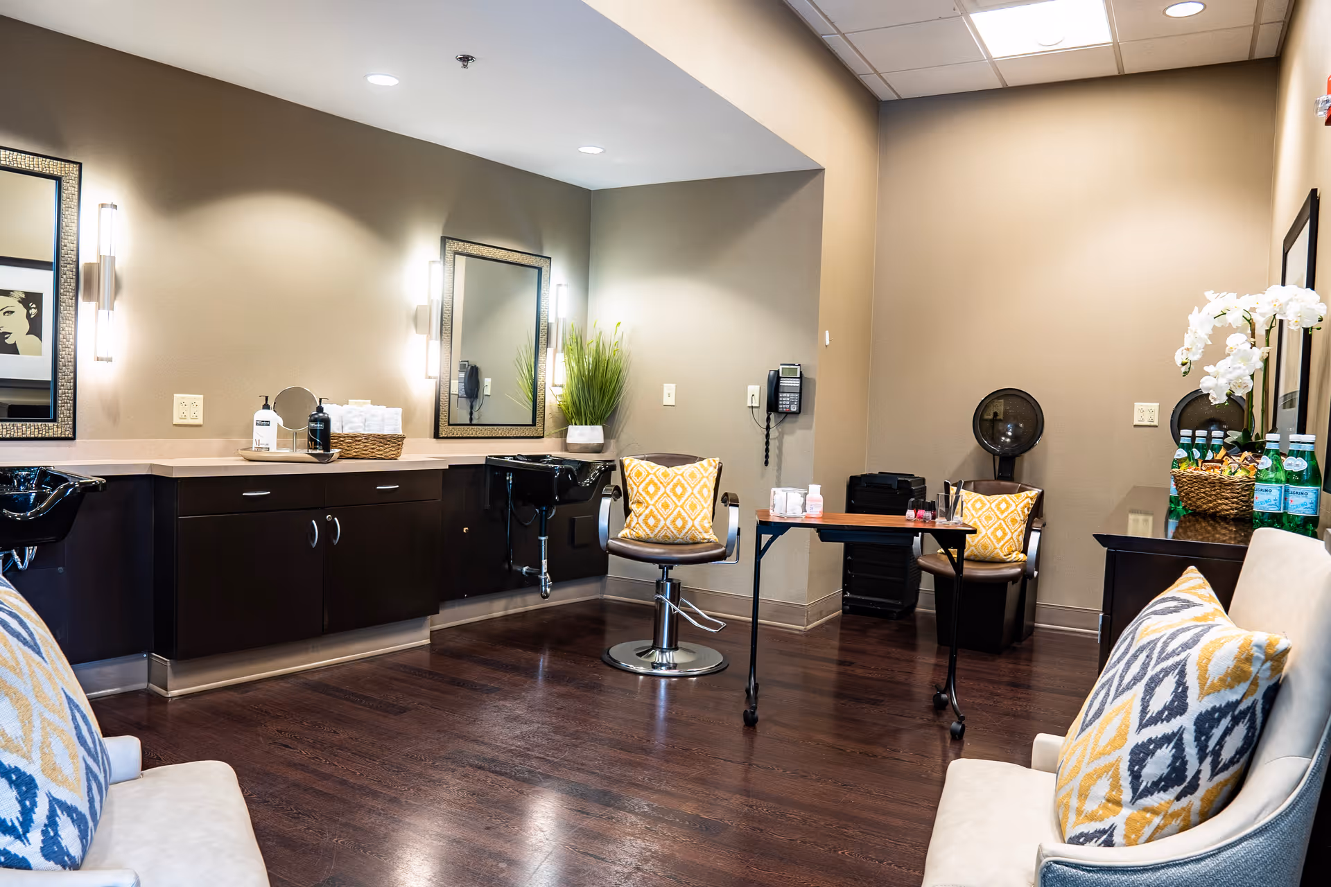 Well-lit salon area with styling chairs, mirrors, wash basins, and seating with patterned pillows.