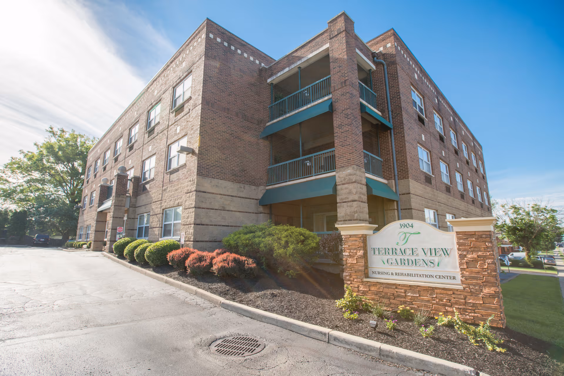 Brick three-story senior living building with balconies and landscaping and a sign reading "Terrace View Gardens" at the entrance.