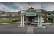 Front exterior view of EverGreen Commons Rehabilitation and Nursing Center showing a covered entrance with white columns, a sign reading 'rehabilitat', and a vehicle parked underneath the entrance canopy. The building is two stories with a combination of brick and siding.