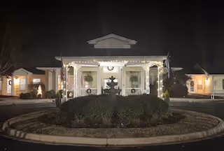 Nighttime exterior view of Summit Place front entrance with circular driveway and landscaped island.