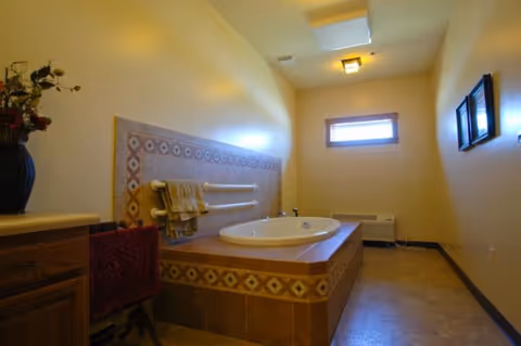Tiled bathroom featuring a raised built-in soaking tub with grab bars, towels, a small window, and a vanity.