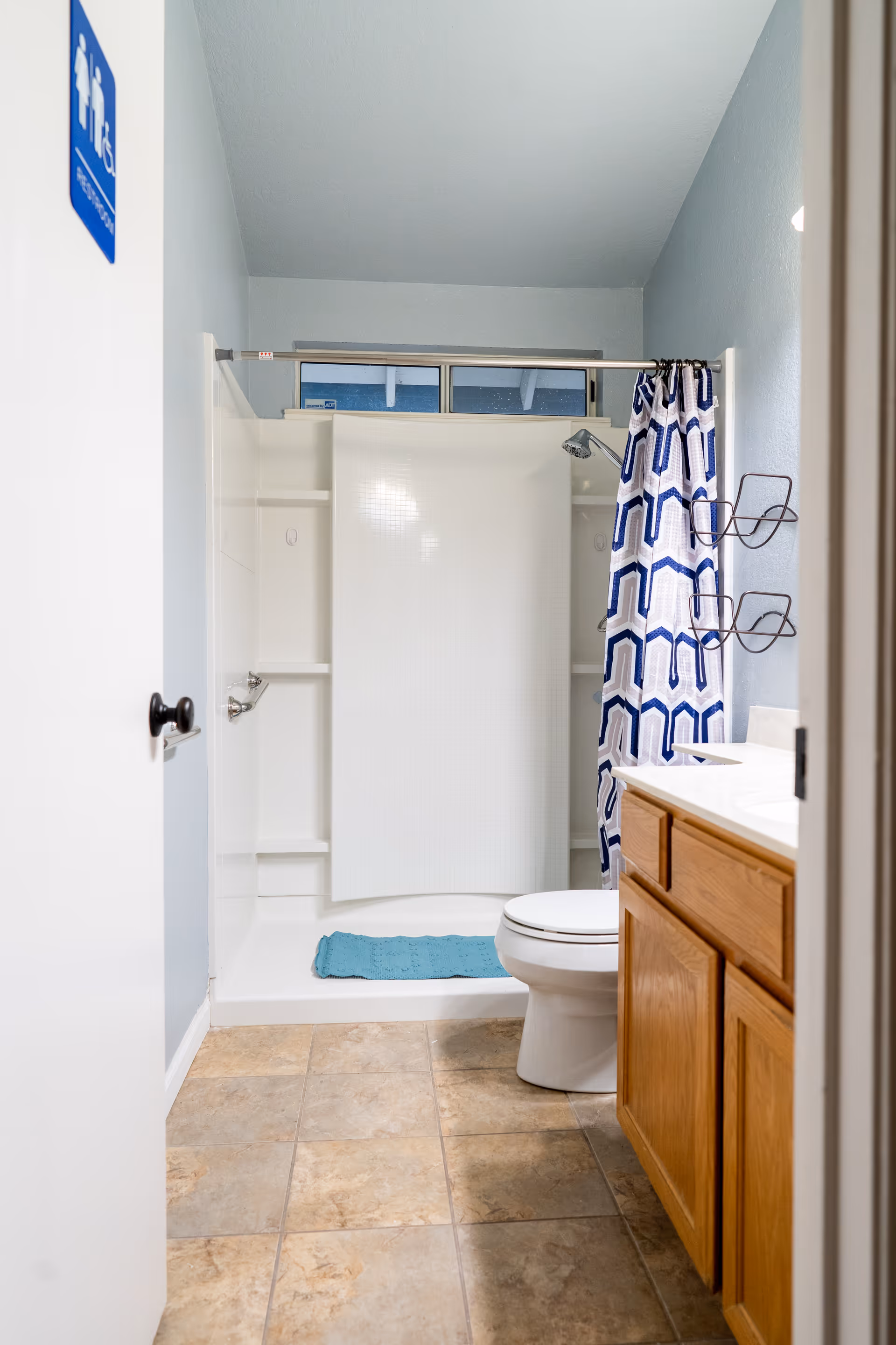 Bathroom with a walk-in shower and blue geometric shower curtain, toilet, sink, and wooden vanity.