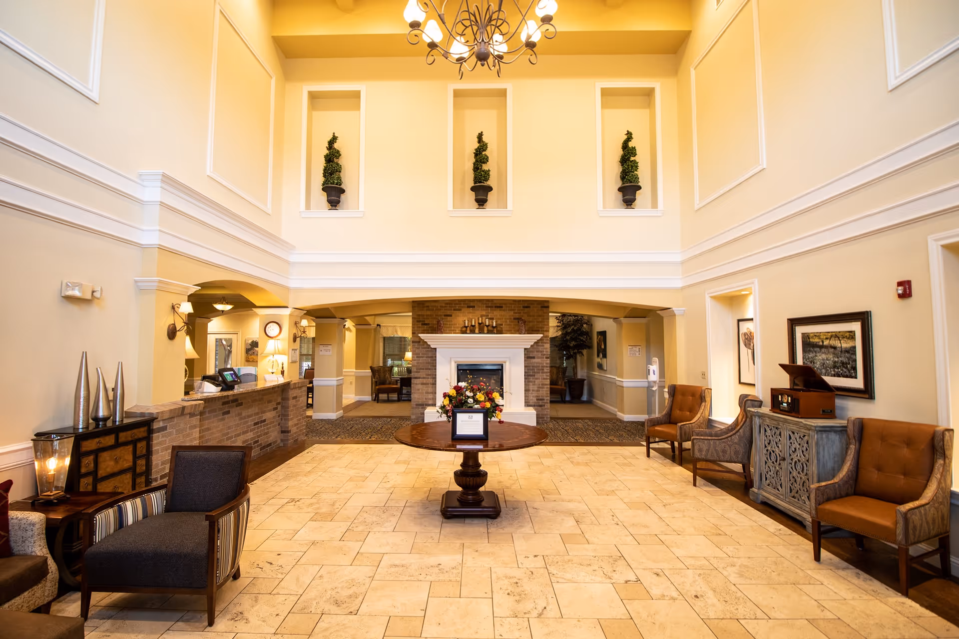 Spacious two-story lobby with a central round table and floral arrangement, fireplace, reception desk, and seating areas.