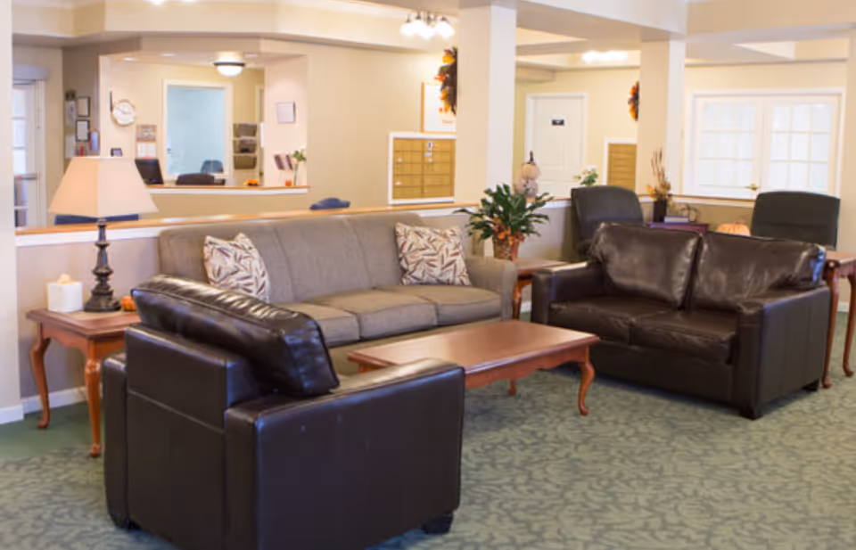 Senior living common area with sofas, leather armchairs, a coffee table and a reception desk in the background.