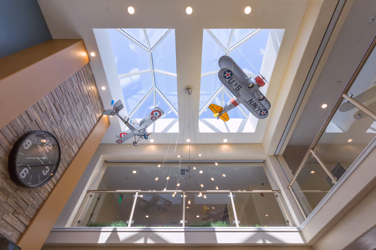 Atrium interior with a skylight, hanging model airplanes, a modern chandelier, balcony railing and a wall clock.