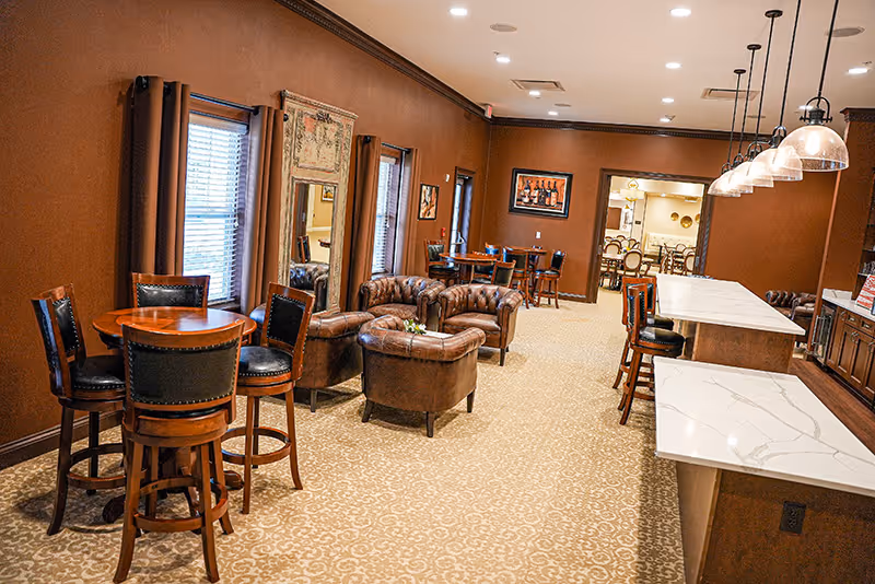 A warm common lounge with leather chairs, high-top tables and a long marble-topped bar under pendant lights.