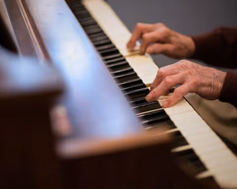 Close-up of elderly hands playing the keys of a wooden piano.