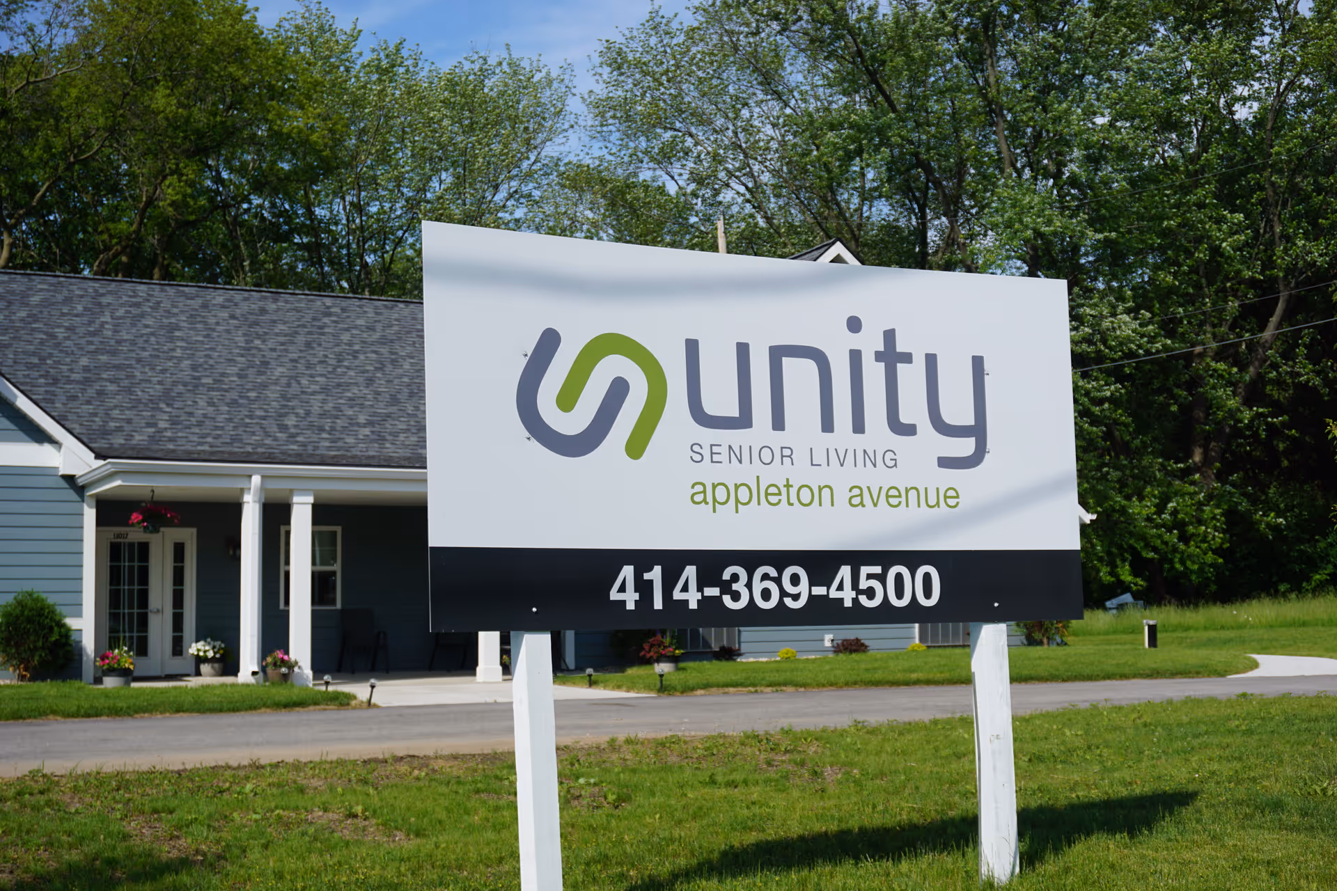 A large sign for Unity Senior Living Appleton Avenue with a phone number stands on the lawn in front of a single-story building.