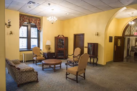 Spacious yellow-walled sitting room with vintage chairs, a patterned sofa, round coffee table, chandelier, and an arched doorway.