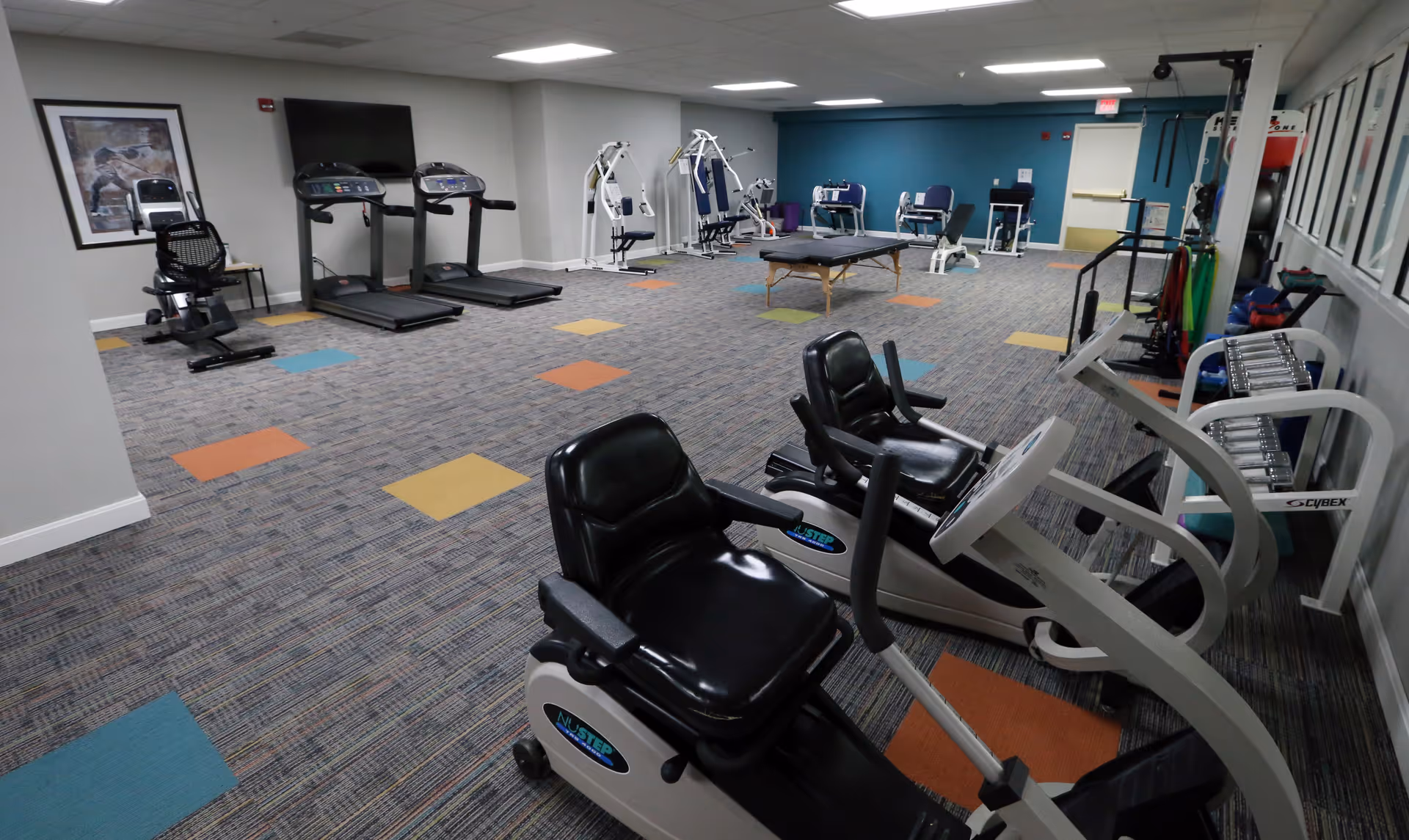 Interior fitness room with treadmills, recumbent bikes, strength machines, free weights, and a treatment table.