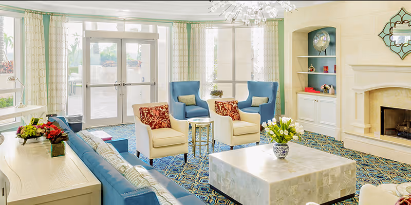 Bright communal living room with sofas and armchairs arranged around a large square coffee table and a fireplace.