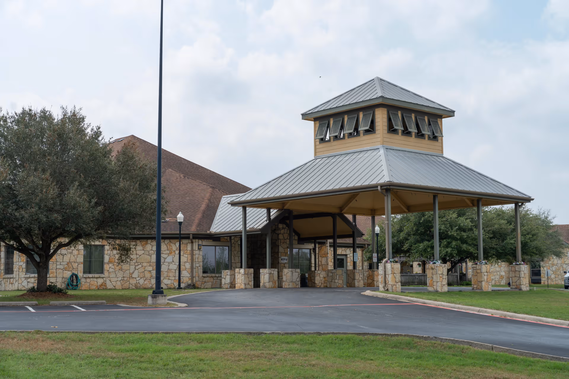 Exterior view of a senior living facility entrance with a stone facade and a large covered porte-cochère.