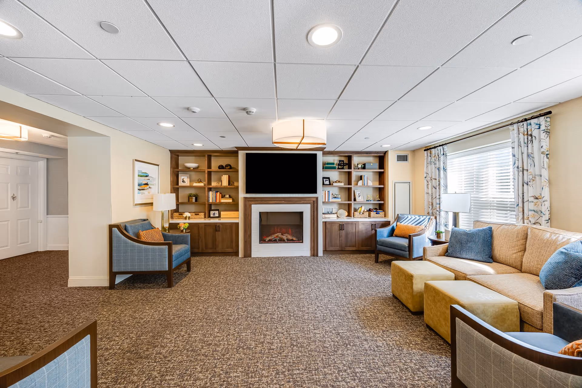 Bright common living room with sofas, armchairs, a fireplace and TV set within built-in shelving.
