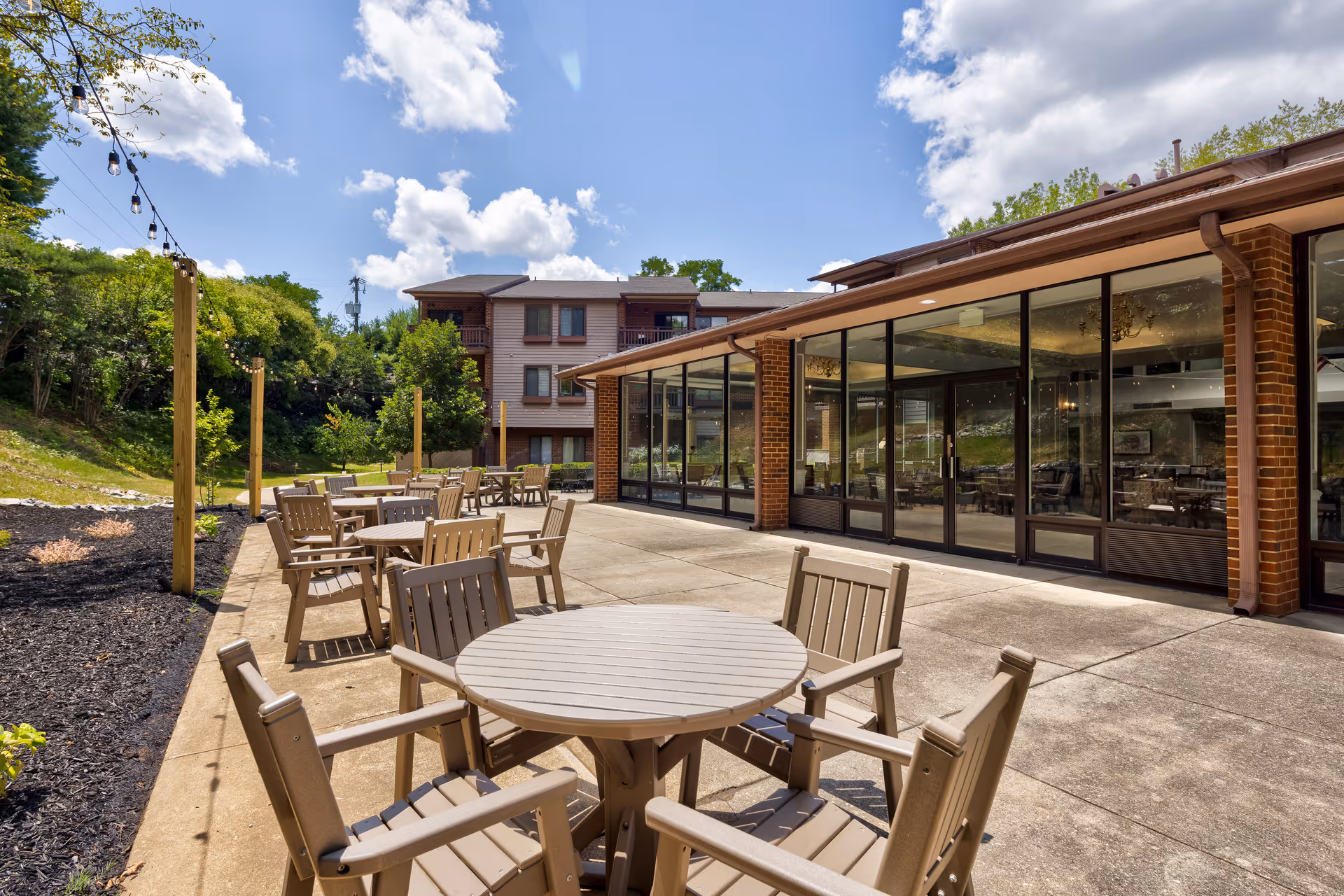Outdoor patio area with round tables and chairs beside a glass-walled building under a blue sky.