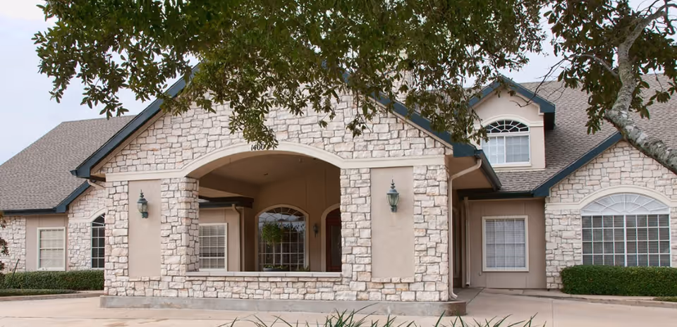 Front exterior of a stone-faced building with an arched covered entrance and multiple windows.