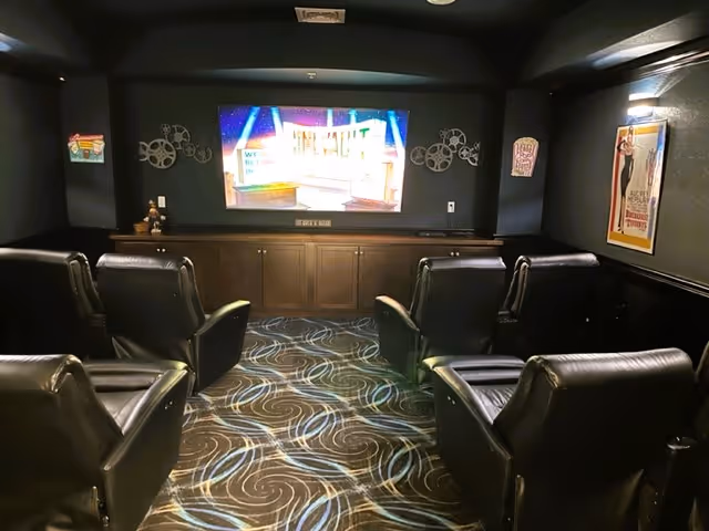 Small darkened theater-style room with six black leather recliners facing a wall-mounted flat-screen TV.