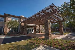 Sunny exterior view of Ivy Springs at Buford entrance featuring stone columns and a wooden canopy