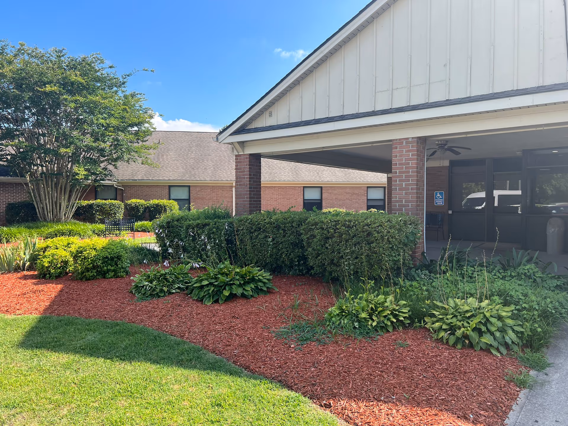 Exterior view of a senior living facility entrance with landscaped bushes and mulch.