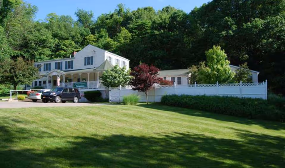 White two-story senior care residence with a front porch, driveway, and green lawn.