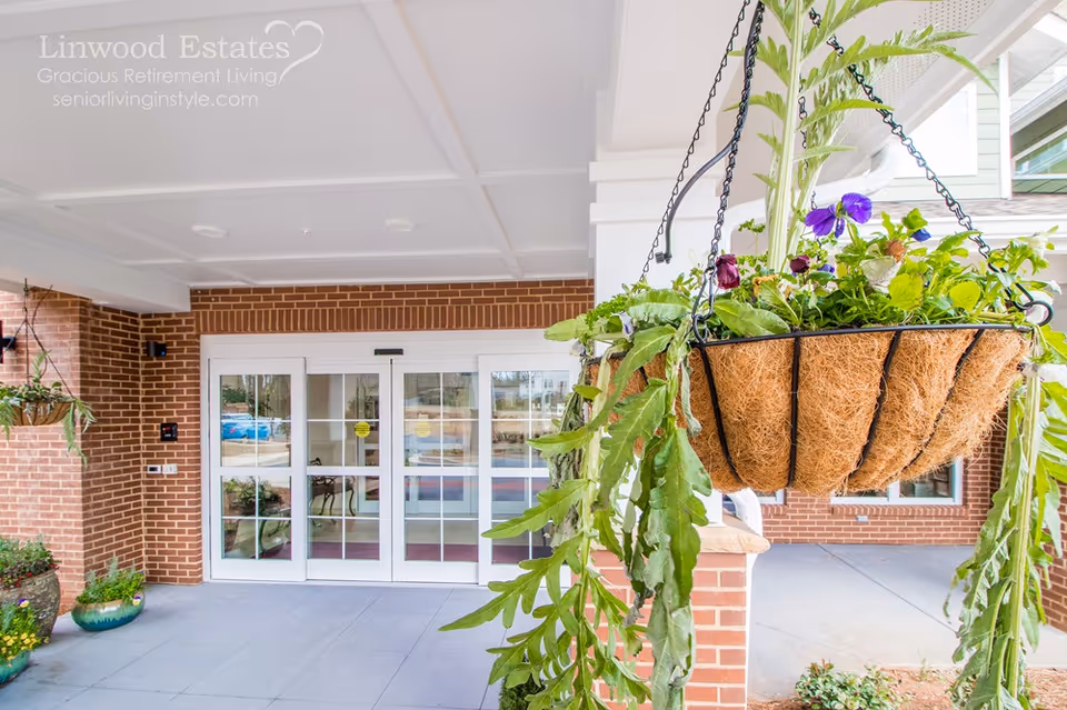 Covered entrance of Linwood Estates with hanging flower baskets in the foreground and sliding glass doors at the building front.