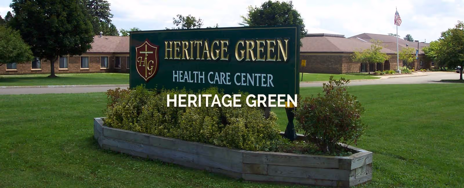 A large green sign reading Heritage Green Health Care Center sits in a planter on a lawn with the facility building in the background.