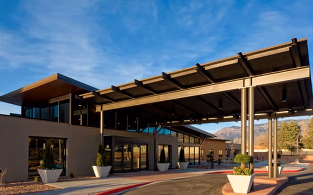 Exterior view of a modern senior living facility building with large windows and a covered entrance area under a clear blue sky.