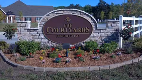 Exterior stone sign for The Courtyards Senior Living with landscaped flower beds in front.