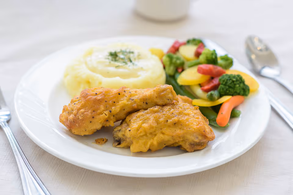 A plate with fried chicken, mashed potatoes and mixed vegetables on a table with utensils.