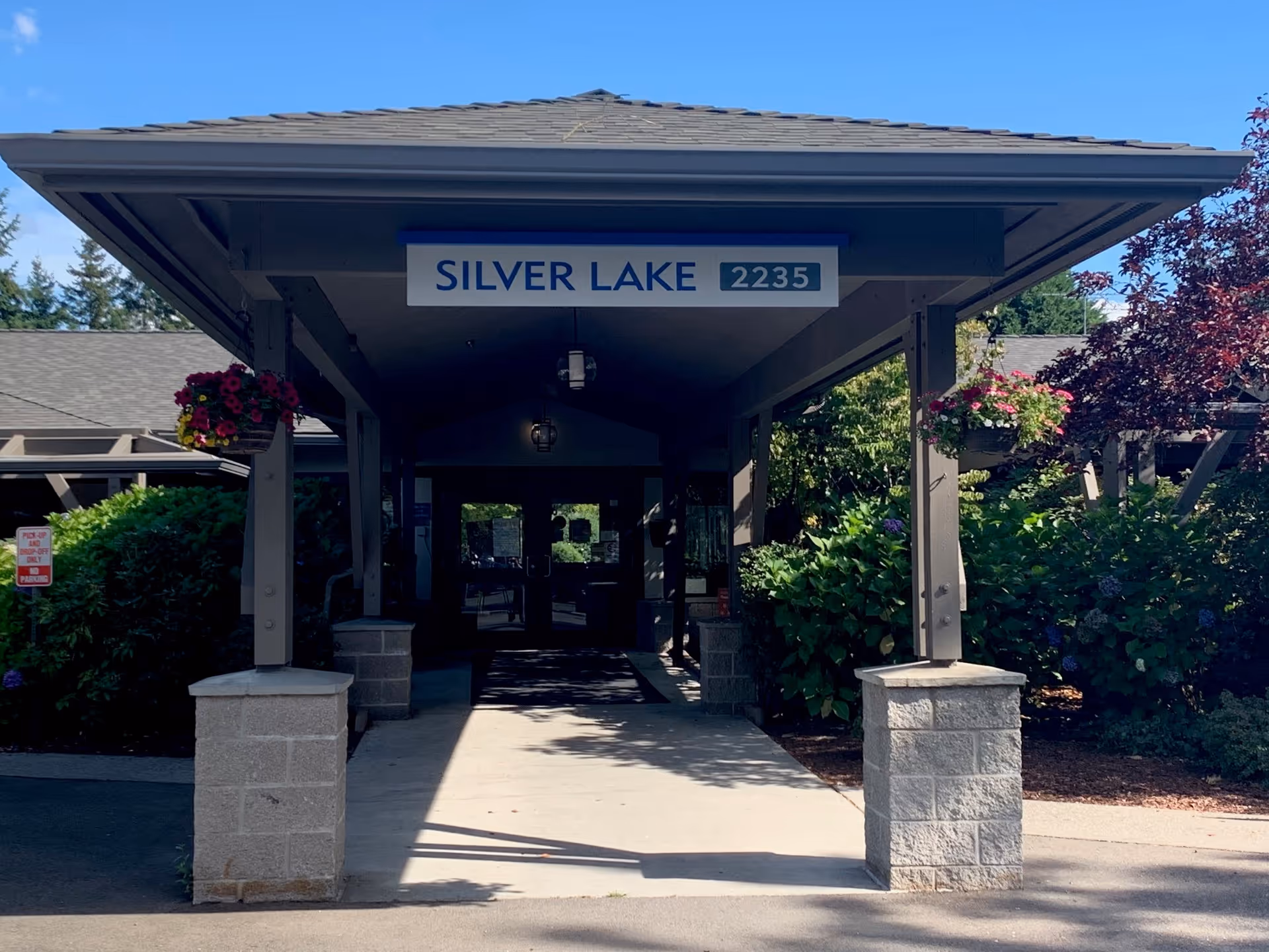 Covered entrance portico of the Silver Lake building with a sign reading "SILVER LAKE 2235" and hanging flower baskets.