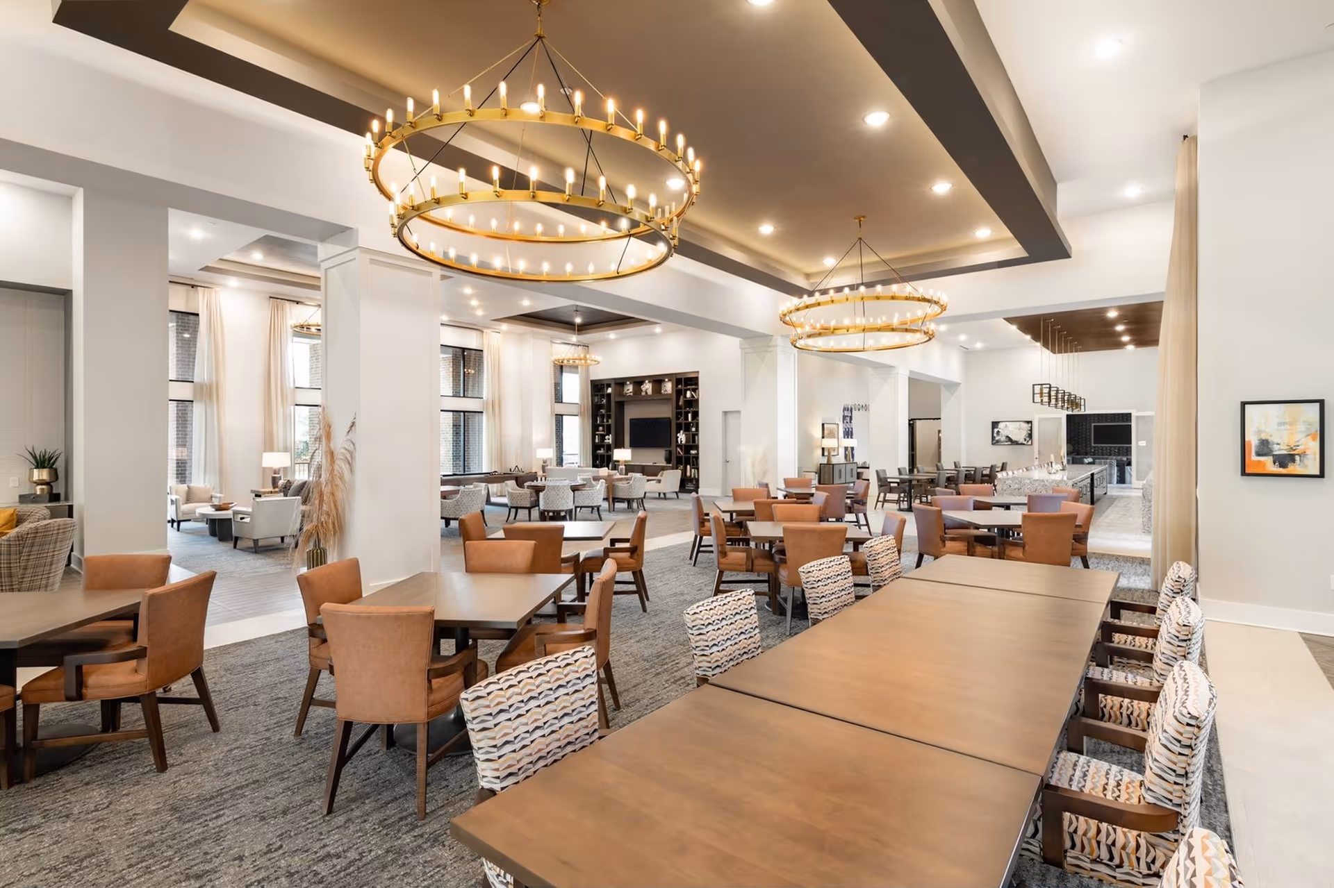 Spacious, elegant communal dining and lounge area with multiple tables, patterned chairs, and large circular chandeliers.