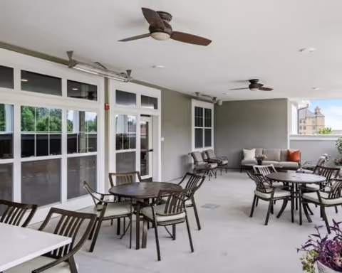 Covered outdoor patio with multiple round tables and chairs, ceiling fans, and sliding glass doors leading inside.