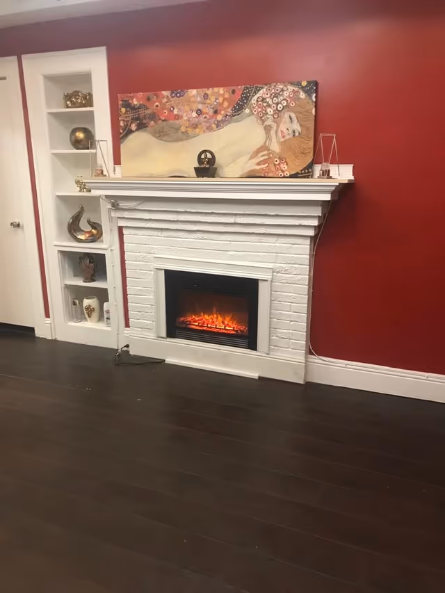 White brick fireplace with an electric fire, a colorful painting on the mantel and built-in shelves against a red wall.
