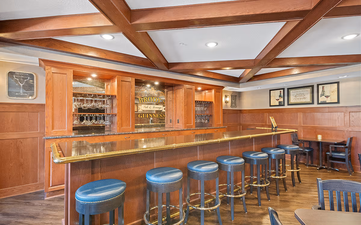 Wood-paneled bar area with a long countertop and a row of blue bar stools under a coffered ceiling.