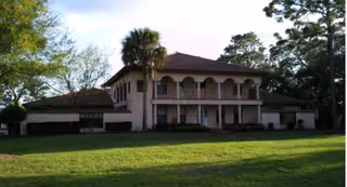 Two-story Mediterranean-style assisted living facility with arches, balcony, and a green lawn.