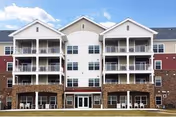 Front view of a multi-story residential building with stacked balconies, a central entrance, and a lawn.