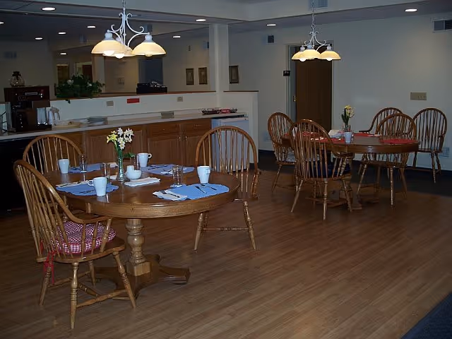 Communal dining room with round wooden tables and chairs set with place settings and pendant lights.