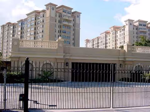 Gated entrance and grand beige multi-story building with balconies, front view of Sarasota Bay Club.
