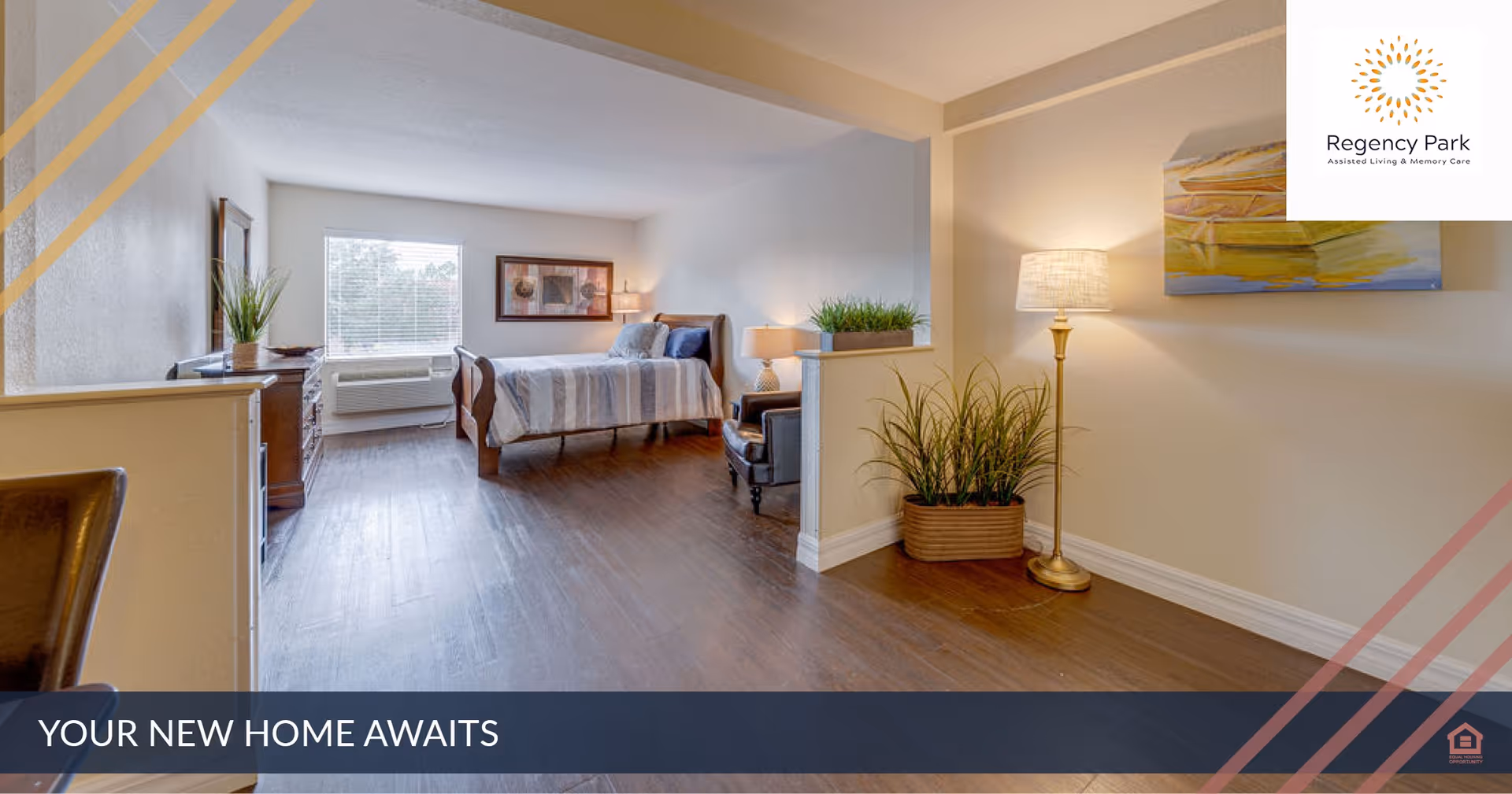 A bright and spacious bedroom in an assisted living facility featuring a bed with striped bedding, a window with blinds, a wooden dresser, a comfortable chair, a floor lamp, and decorative plants. The room has wooden flooring and light-colored walls with artwork and a large open layout.