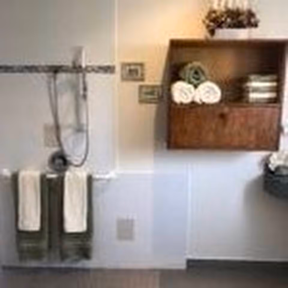 Bathroom wall with a handheld showerhead, a towel rack holding two folded towels, and a wooden wall shelf with rolled towels and decor.