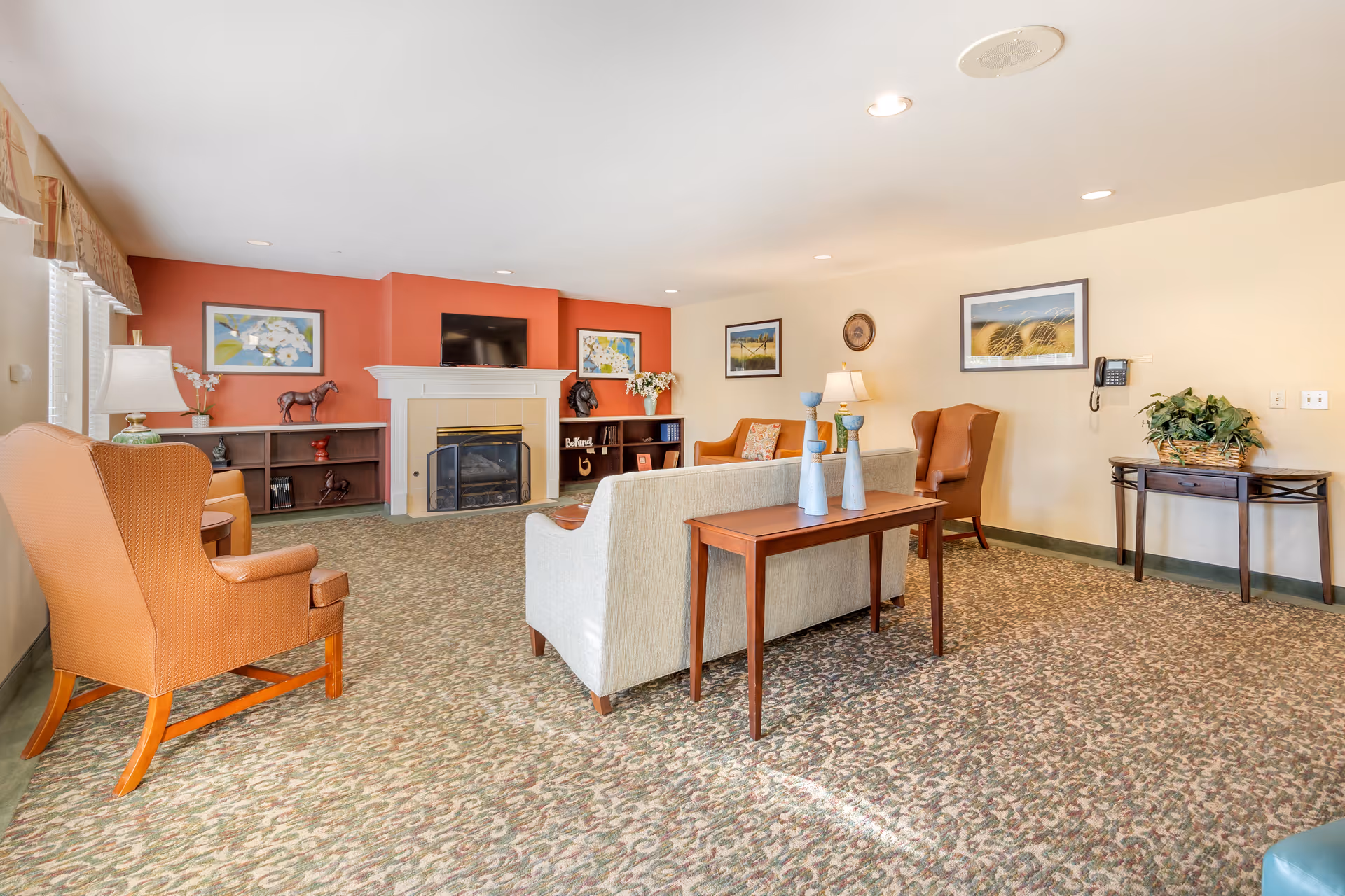 Comfortable communal living room with sofas and armchairs arranged around a fireplace and wall-mounted TV.